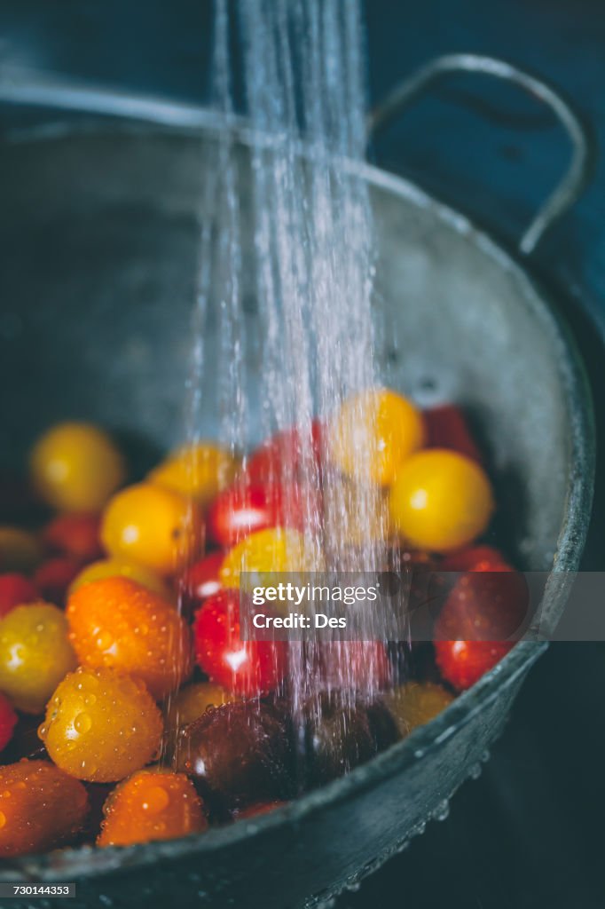 Cherry tomatoes in a colander under running water