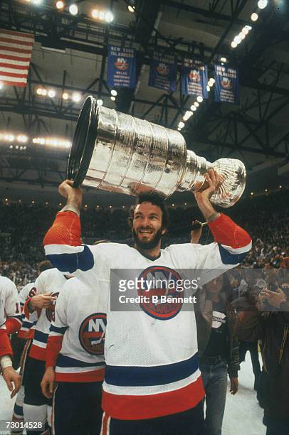 American professional ice hockey player Ken Morrow of the New York Islanders lifts the Stanley Cup over his head after his team won the NHL...