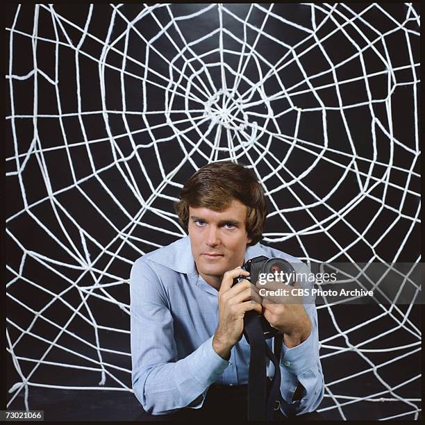 Promotional portrait of American actor Nicholas Hammond, as Peter Parker , as he holds a camera and sits in front a large 'web' for the CBS...