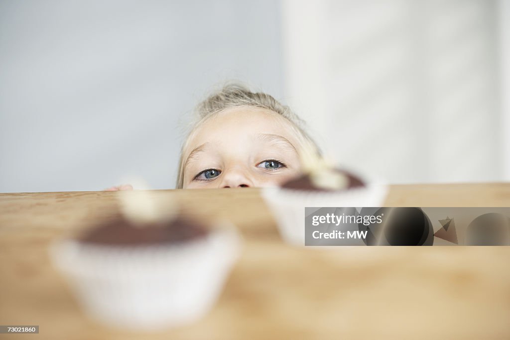 "Girl (5-7) looking at cupcakes on counter, high section"