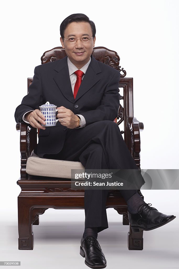 Businessman sitting, holding cup of tea, portrait