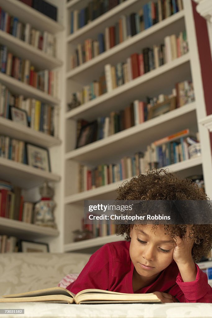 Girl (6-7) lying on couch, reading book