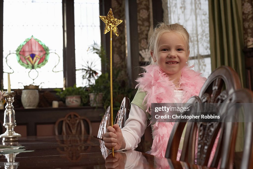 Smiling girl (6-7) wearing feather boa holding magic wand in living room