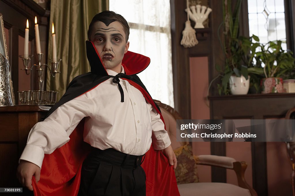 Boy (6-7) dressed as vampire posing in living room, portrait, close-up