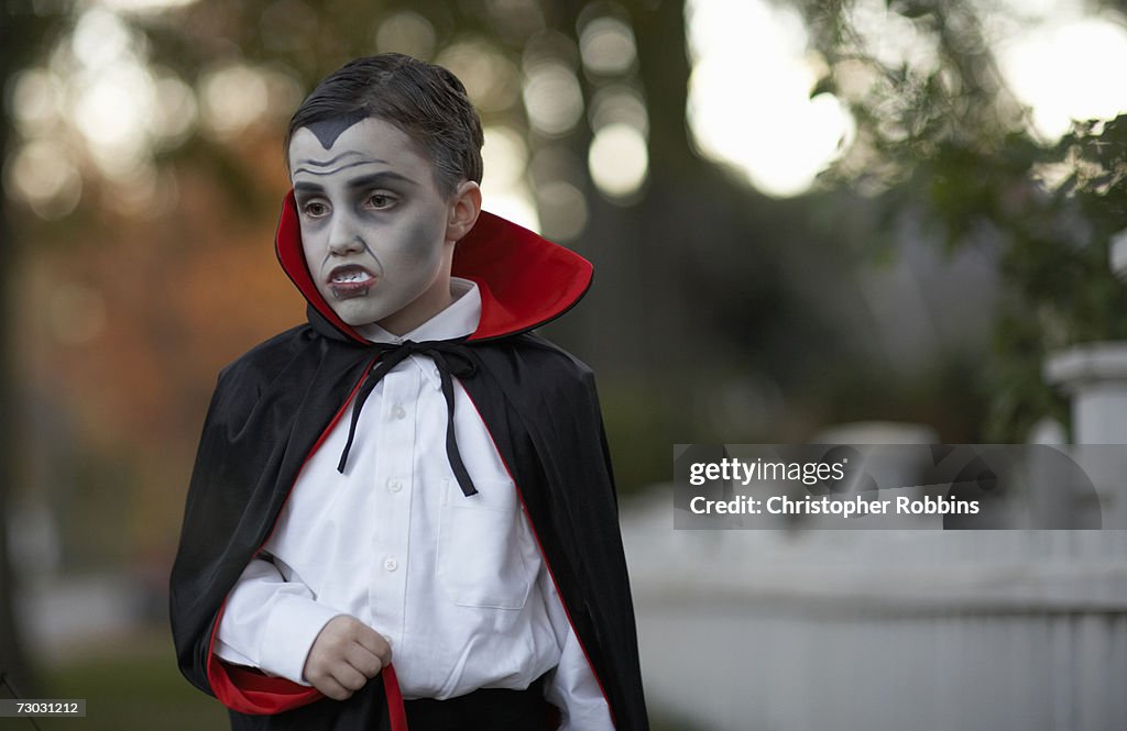 Boy (6-7) dressed as vampire standing outdoors