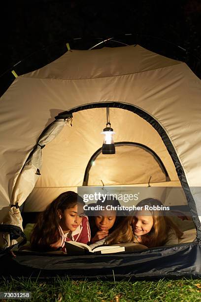 three girls (10-11, 12-13) lying in tent, reading book at night - jack o lantern fotografías e imágenes de stock