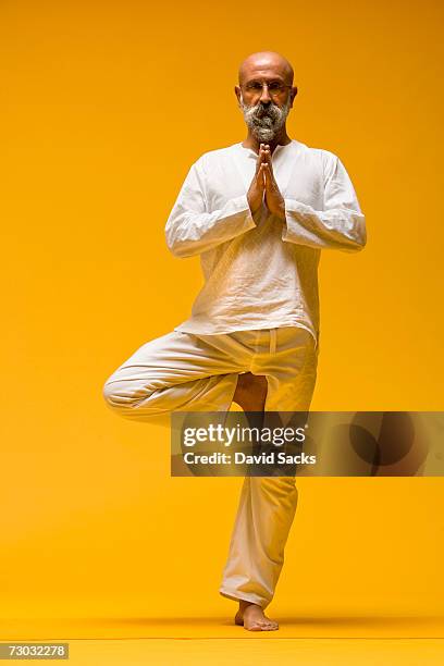 yoga teacher balancing on one leg in tree pose, front view - front on portrait older full body stock-fotos und bilder