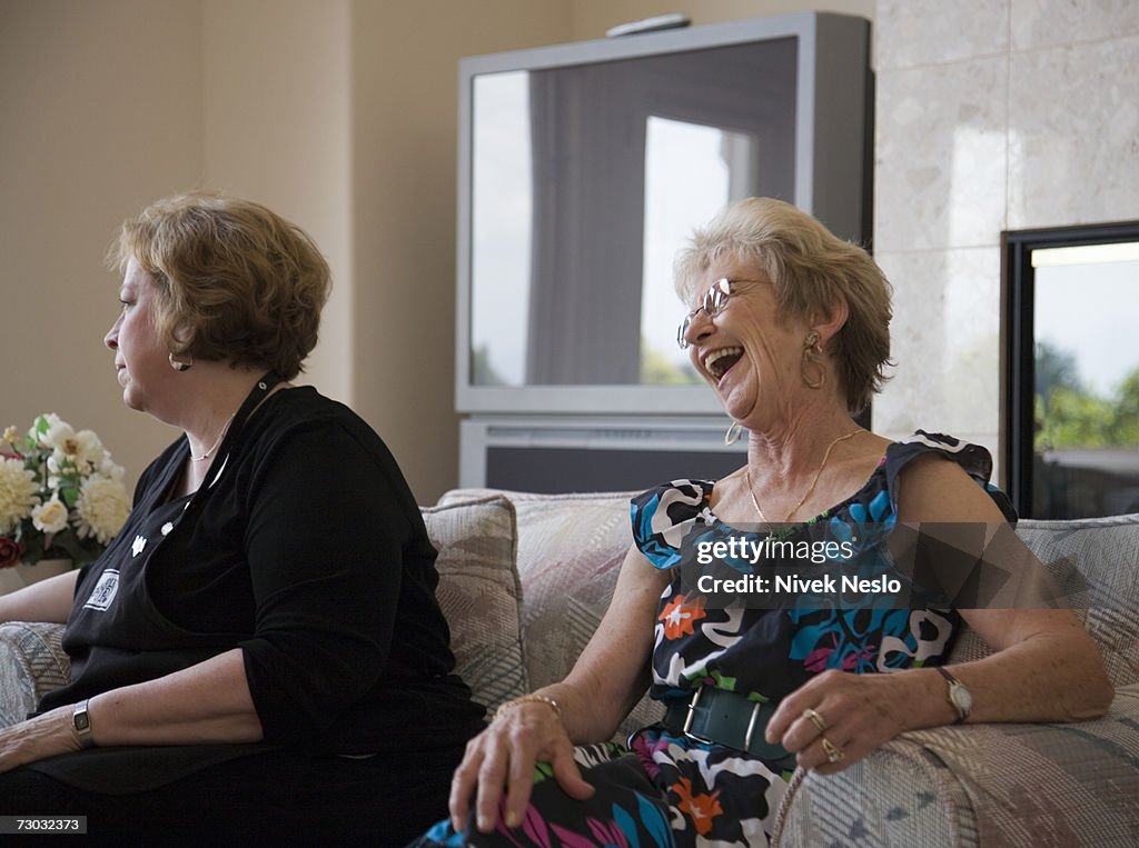 Two senior women sitting on couch, laughing
