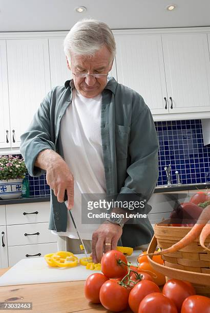 senior man cutting pepper in kitchen - mature men foto e immagini stock