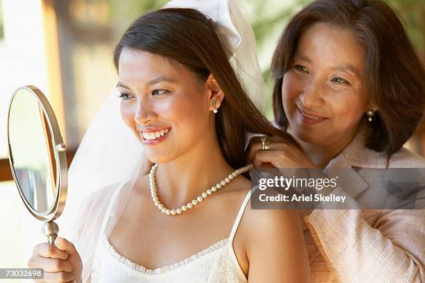 mother fastening pearls necklace on bride looking at hand mirror - daughter wedding stock pictures, royalty-free photos & images