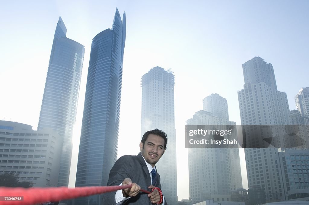 Businessman tugging rope, Towers seen through the mist in the background