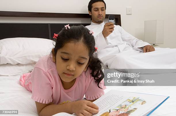 daughter reading on the bed while father is using his cell phone - hot middle eastern girls stock-fotos und bilder