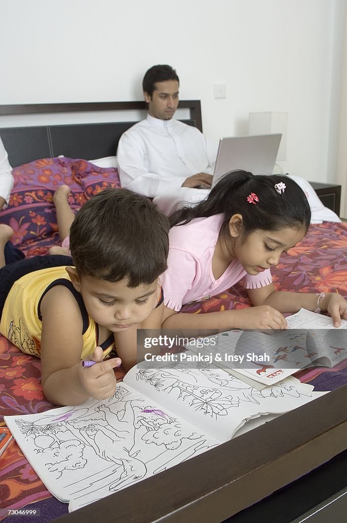 Children reading on the bed while father works