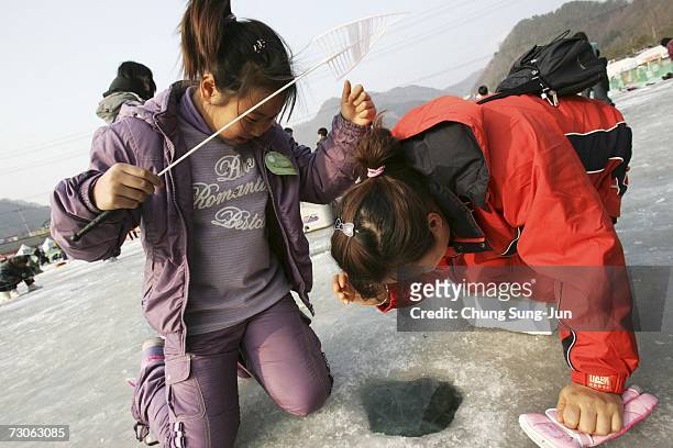 Mother and daughter cast lines through holes into a frozen river during a contest to catch Mountain Trout on January 22, 2007 in Hwacheon, South...