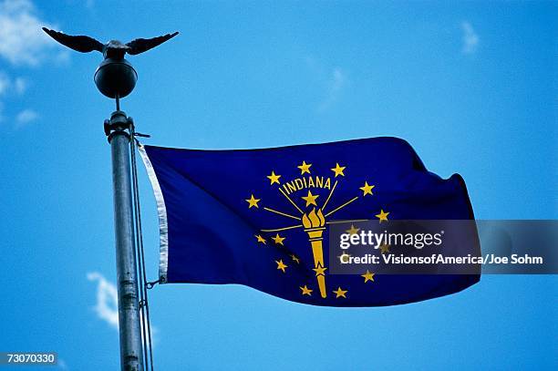 this is the state flag waving in the wind. it is on a flagpole against a blue sky. it has stars surrounding a symbol at the center. - indiana flag stock pictures, royalty-free photos & images