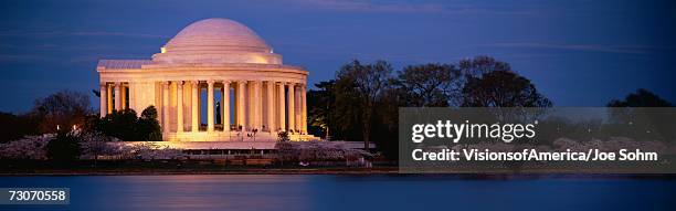 this is the jefferson memorial next to the tidal basin. cherry blossoms are blooming on the trees surrounding it at dusk. - jeffersonmonumentet bildbanksfoton och bilder