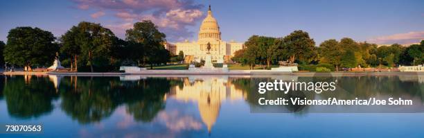 "this is the u.s. capitol showing the west side view at sunset. the capitol is in front of the reflecting pool, showing a reflection of itself in the pool. the capitol is surrounded by green trees and a blue sky with a public statue in front of it." - washington dc bildbanksfoton och bilder