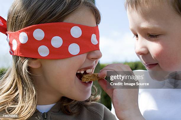 boy feeding biscuit to girl in a blindfold - kid mouth open stock pictures, royalty-free photos & images