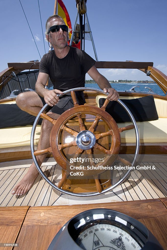 Captain at the helm of sailboat, compass in foreground