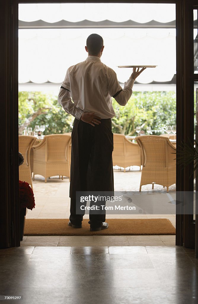 Waiter carrying tray in restaurant, rear view