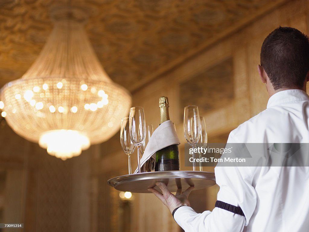Waiter carrying Champagne on tray in hotel, rear view