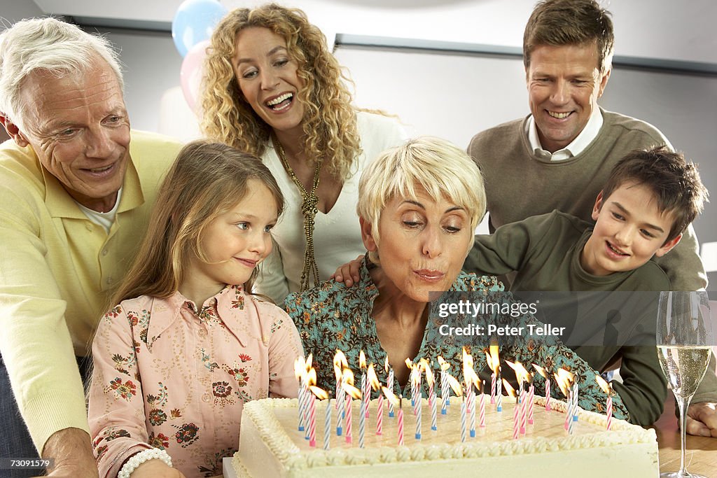 Three generational family with children (5-10 years), grandmother blowing out candles on birthday cake