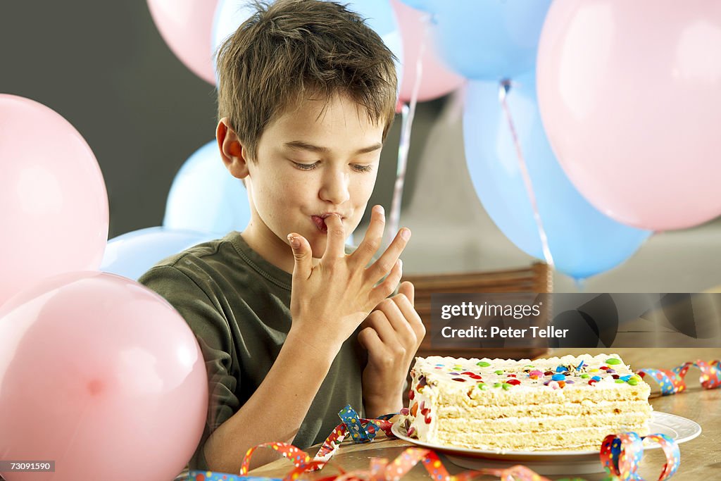 Young boy (10-11 years) with birthday cake, licking fingers