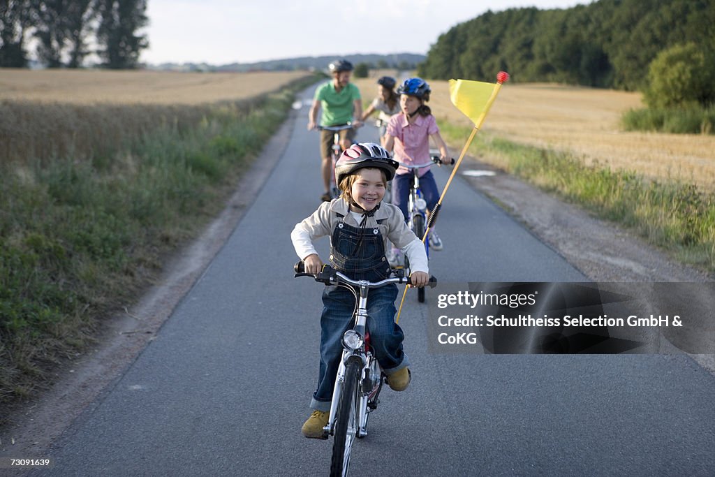 Father with three children (6-11) riding bicycles on country road