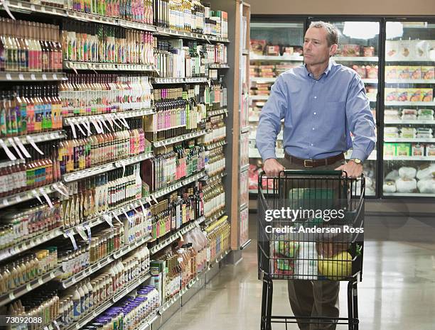 man pushing shopping trolley in store aisle - spingere carrello foto e immagini stock