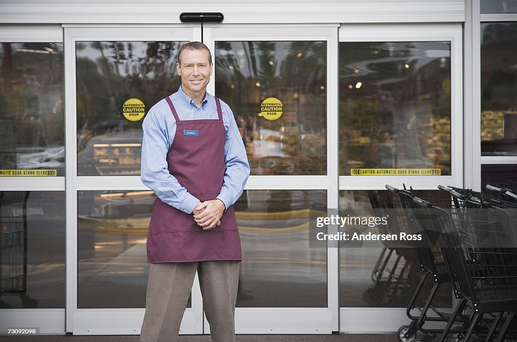 Male shop assistant standing in front of shop doors, portrait