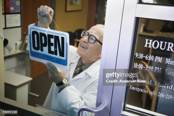 senior male pharmacist hanging 'open' sign in shop door, elevated view - opening hours sign stock pictures, royalty-free photos & images