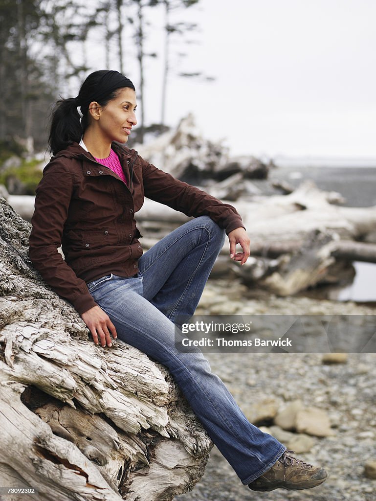 Young woman sitting on tree trunk on beach