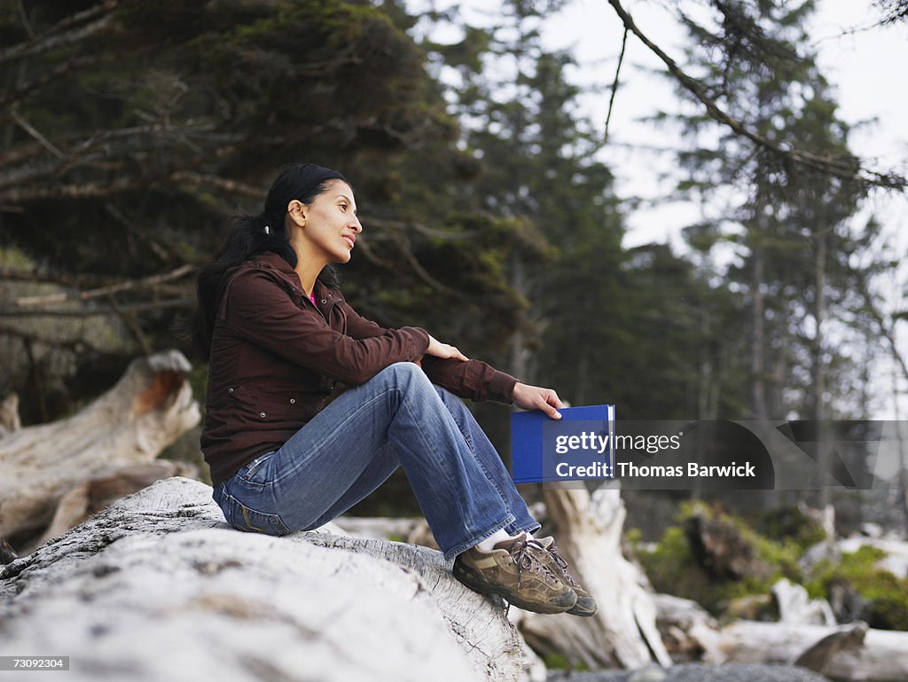 Young woman sitting on log on beach, with book