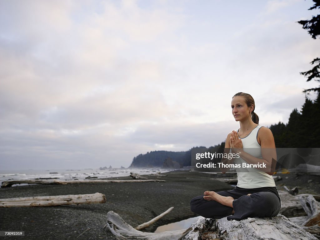 Woman sitting on rock on beach, practicing yoga