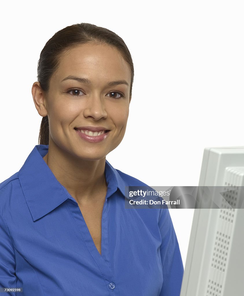 Young woman at computer monitor, smiling, portrait