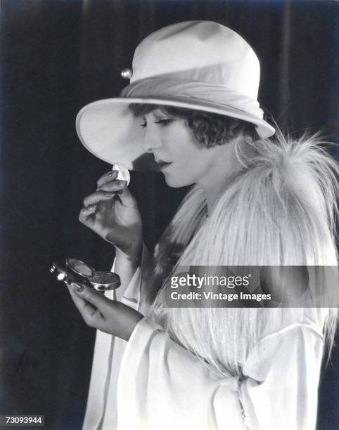 American silent film actress Claire Windsor , born Clara Viola Cronk, looks in a compact mirror case as she applies make-up to her face and wears a...