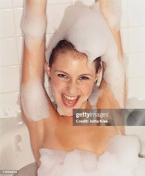 young woman in bubble bath with arms raised - woman bath bubbles stock-fotos und bilder