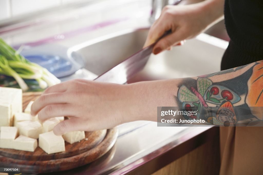 Woman chopping tofu in kitchen with ornate tattooed arm