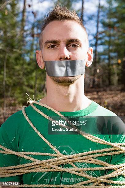 man standing in the woods bound in rope and with adhesive tape covering his mouth - bound and gagged stock-fotos und bilder