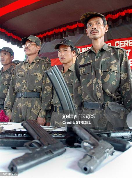 Assault rifles and small arms lie on display as militants stand behind them during a surrender ceremony in Teliamura, 45 km east of Agartala, capital...