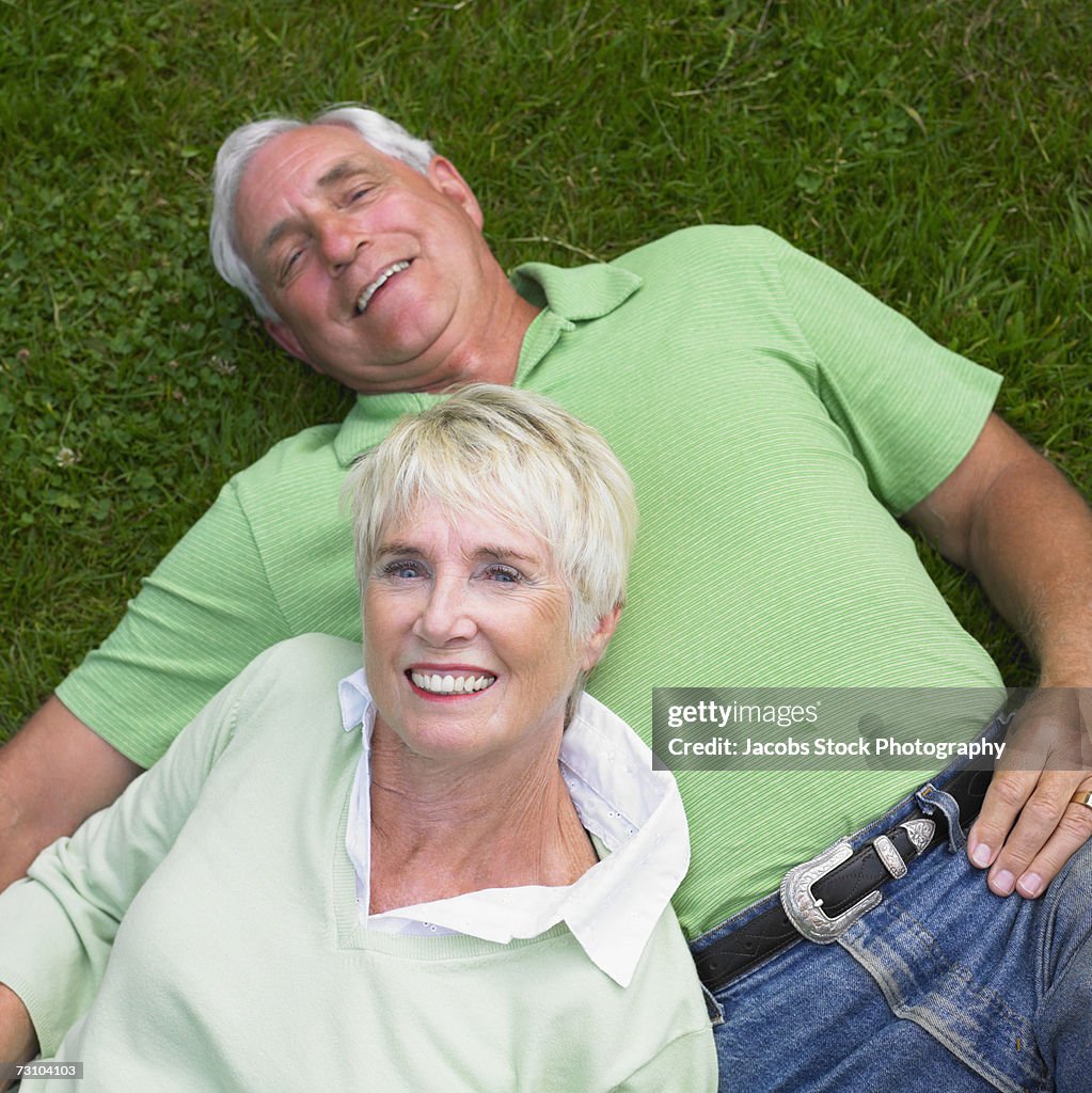 Senior couple lying on grass, smiling, overhead view