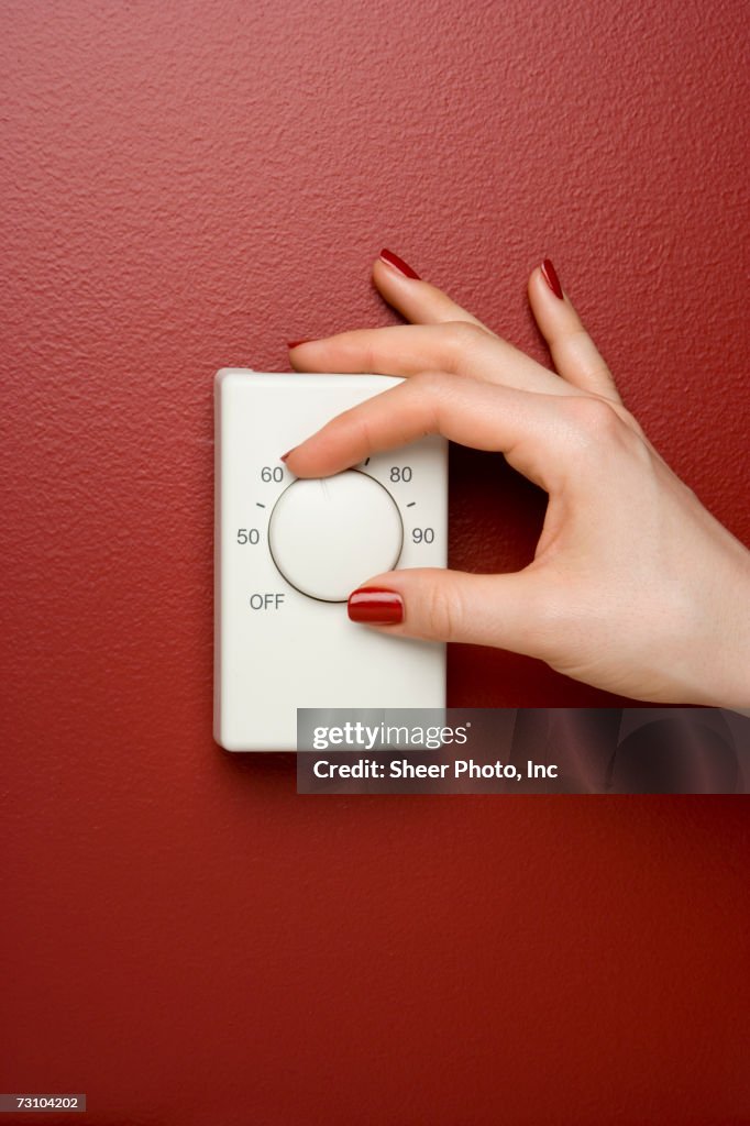Woman adjusting thermostat, focus on hand, close-up