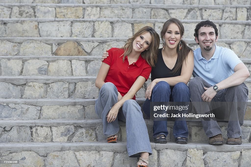 Portrait of two young women sitting on stone steps with a young man