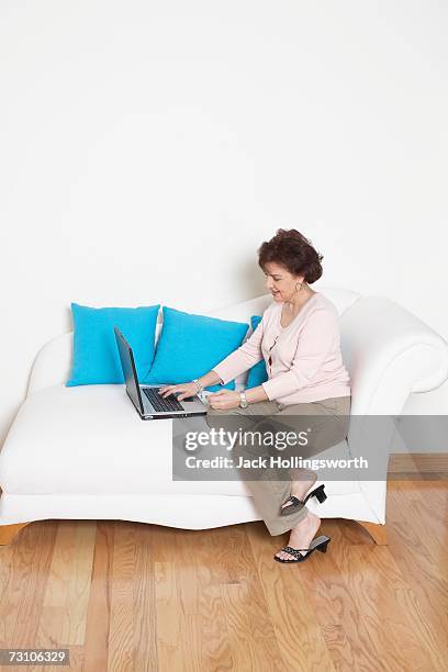 side profile of a senior woman sitting on a couch and using a laptop - profile laptop sitting stock pictures, royalty-free photos & images