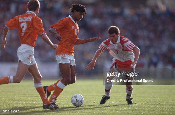 Dutch footballer Frank Rijkaard advances with the ball, supported by teammate Adri van Tiggelen as Danish footballer John Jensen moves in for a...