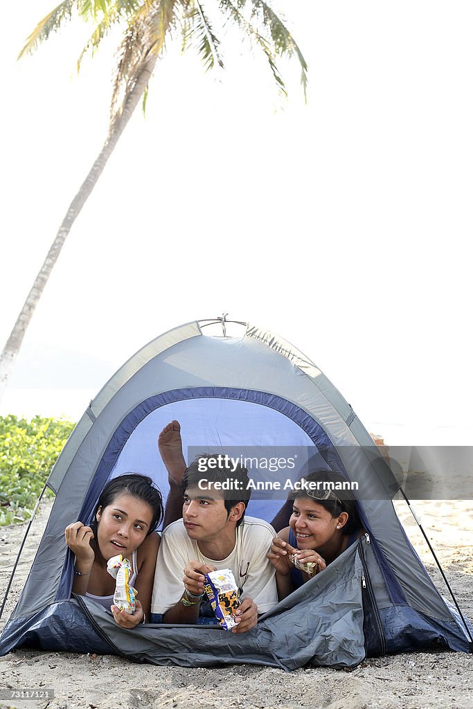Teenagers (15-17) eating candybars in tent on beach