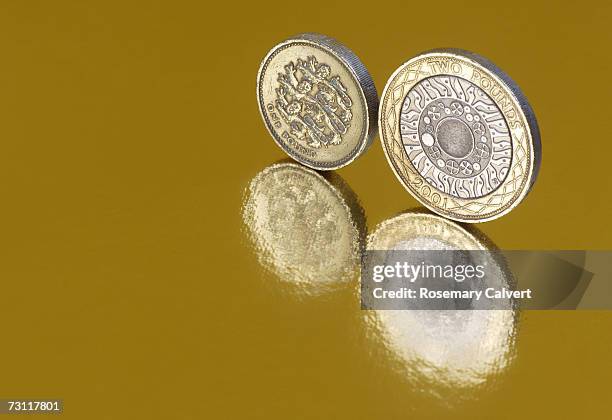 one and two pound coins standing on sides, reflected in gold surface, close-up - two pound coin stock pictures, royalty-free photos & images