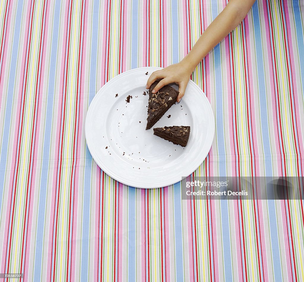 Girl (8-9) taking large slice of cake from plate on table