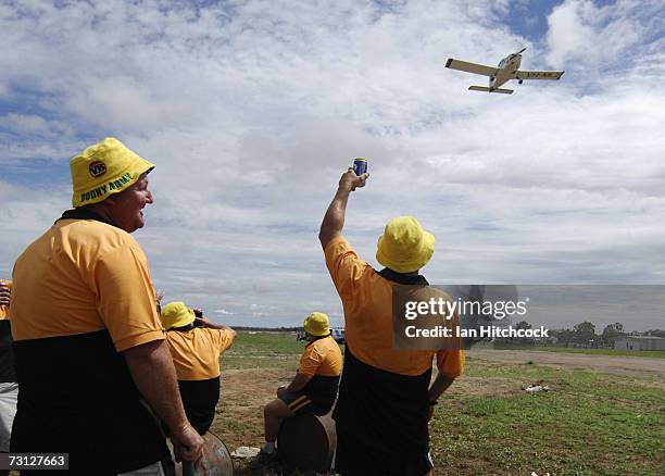 Members of the team 'Coral Coast Marine Madmans' wave to a plane that has just taken off over their cricket pitch during the Goldfield Ashes January...