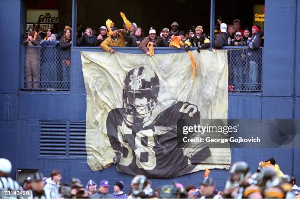 Pittsburgh Steelers fans wave Terrible Towels and cheer while standing near a banner depicting former Steelers linebacker Jack Lambert during a game...